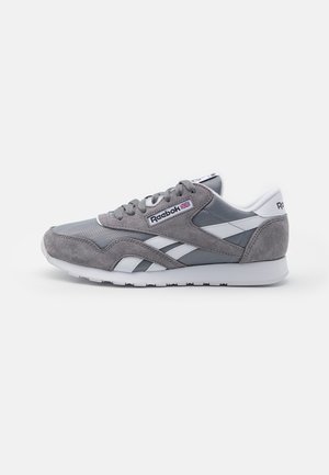 Gray and white Reebok sneaker with suede and mesh panels, lace-up front, and branded logo on side and heel.