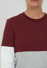 Burgunder og grå fargeblokket sweatshirt med rund hals, myk tekstur og hvite detaljer på ermene. Uformell design, uten synlige mønstre.