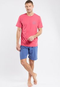 T-shirt rose pour hommes avec un logo bleu circulaire, associé à un short bleu, présentant un design simple et un tissu doux, adapté à une tenue décontractée.
