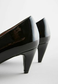 Musta patenttimuovinen korkokenkä, jossa on teräväkärkinen design ja ohut stiletto-korko, esitellen kiiltävää pintakäsittelyä ja sileää tekstuuria.