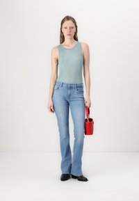 Light blue ribbed tank top, fitted at the torso. Medium wash flared jeans with a classic five-pocket design. Holding a small red handbag.