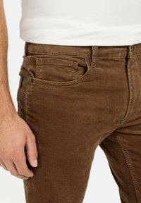 Pantalons en velours côtelé marron avec une coupe ajustée, des stries texturées, un style classique à cinq poches et une fermeture à bouton.