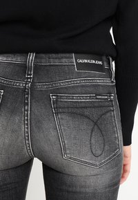 Black denim jeans with a faded gray wash, featuring signature back pockets and a visible Calvin Klein Jeans label at the waistband.