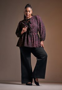 Mustikka leopardikuvioinen paita, jossa on puffihihat, vyötärösta kireä ja kauluksessa nauhakoriste, yhdistetty leveälahkeisiin mustiin housuihin ja mustiin kenkiin.