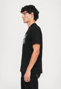 Svart t-skjorte med korte ermer og rund hals, med et hvitt grafisk design på forsiden. Laget av myk bomull, har en avslappet passform.