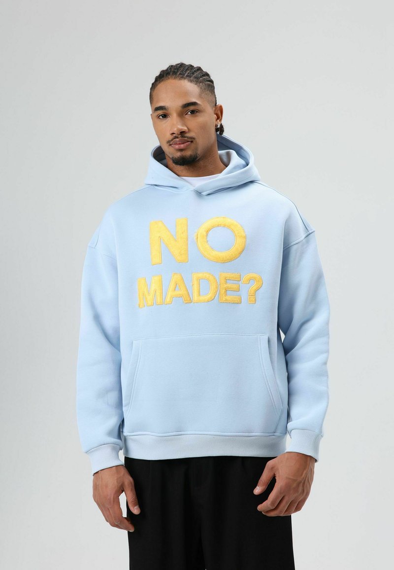 Sweat à capuche bleu clair en matière molletonnée. Présente un grand texte brodé jaune "NO MADE?" sur le devant et une poche kangourou.