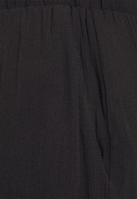 Pantalon à taille élastique noire avec poche latérale visible et tissu texturé.