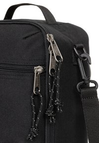 Borsa in tessuto nero dalla forma rettangolare, con cerniere argentate, esterno testurizzato e tracolla rimovibile con dettagli in metallo.