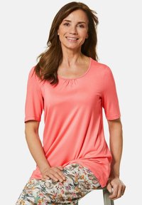 Koraalkleurig t-shirt met korte mouwen, een ronde hals en plooidetails, gecombineerd met bloemenpatroon broek met vlinders en bladeren.