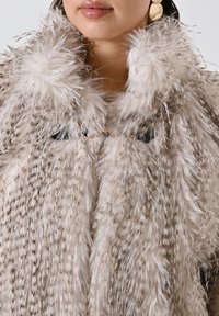 Faux-Fur-Mantel in hellem Beige mit dunklen Streifen, ausgestattet mit einem flauschigen Kragen und Hakenverschluss. Die weiche Textur verleiht dem Design Tiefe.