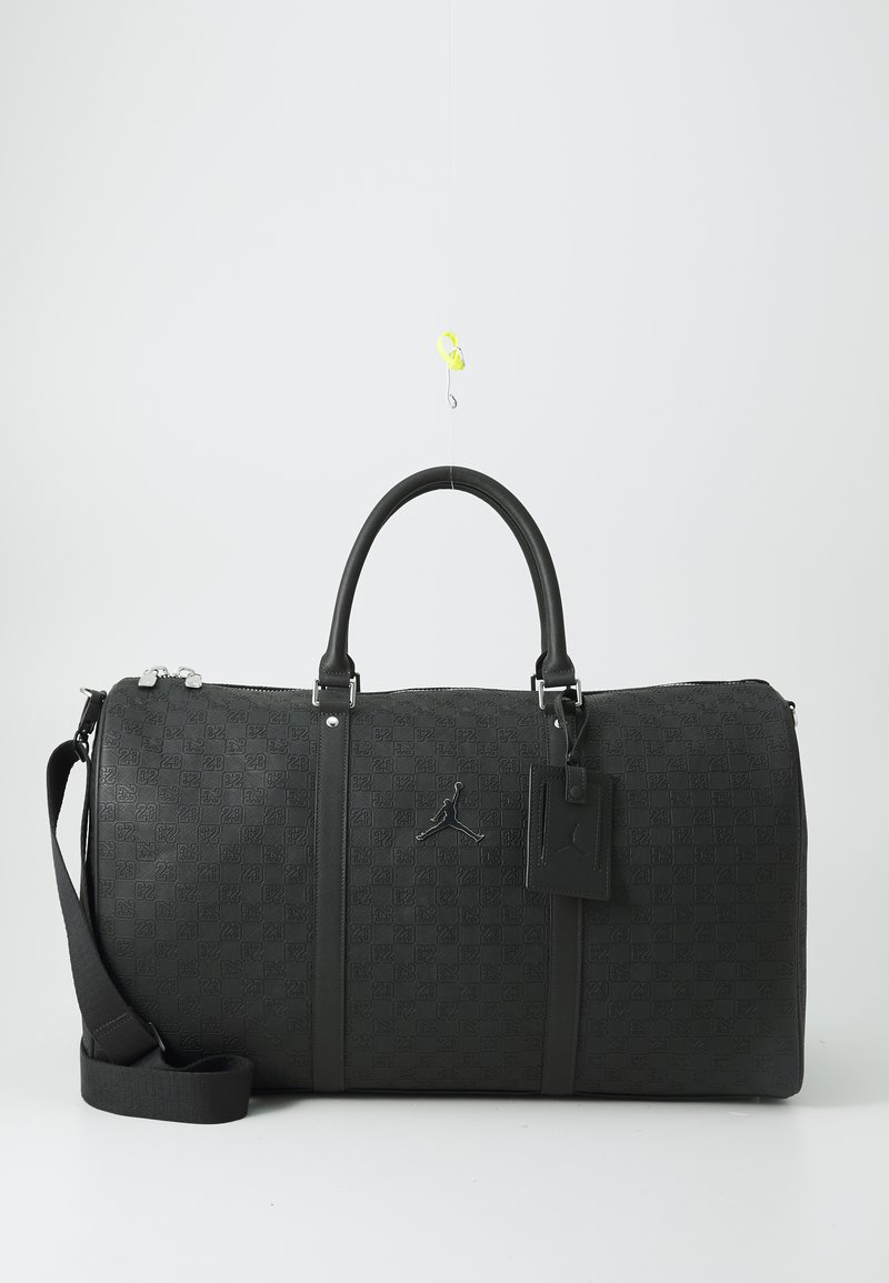 Borsa duffle nera con motivo in rilievo, texture liscia, manici doppi, tracolla sganciabile e un'etichetta con un logo. Accenti in metallo argentato.