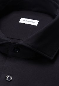 Camicia nera con colletto, bottoni superiori abbottonati, che mostra l'etichetta bianca del marchio "seidensticker" all'interno del colletto.