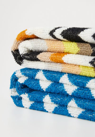 Sett med tre rullte håndklær i teksturert bomull, med mønstre: toppen i oransje, svart og beige; bunnen i blått med hvite diamanter.