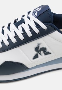 Sneaker navy e bianche con tomaia in pelle liscia, lacci bianchi e logo sul linguetta. Suola piatta in gomma con dettagli azzurri.