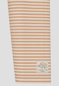 Gestreepte stof in zachte beige en crèmekleuren, met een getextureerd ribpatroon. Een klein gestikt label met een egelsymbool is zichtbaar.