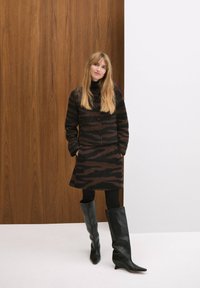 Brown and black striped coat with high collar and buttons, paired with a similar patterned skirt and knee-high black leather boots.