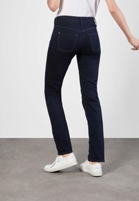 Marineblå bukser laget av elastisk stoff, med smal passform, fire lommer og kontraststing, kombinert med hvite sneakers.