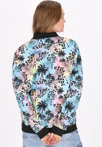 Giacca bomber colorata con una stampa tropicale pastello che presenta palme e macchie di leopardo; colletto e polsini a costine neri.