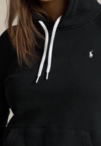 Černá bavlněná mikina s bílými šňůrkami, na hrudi s malým vyšitým logem a s přední klokaní kapsou.