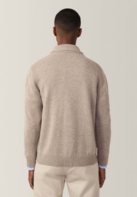 Beżowy sweter robiony na drutach z kołnierzem szalowym, z prążkowanymi mankietami i dołem, o gładkiej fakturze i luźnym kroju, widziany z tyłu.