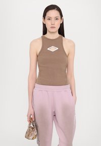 Ruskea ilmanhihoilla bodysuit, jossa on valkoinen timantinmuotoinenleikkuu, yhdistettynä vaaleanpunaisiin collegehousuihin ja pieneen kuviolliseen laukkuun. Sujuva, uritettu pinta.