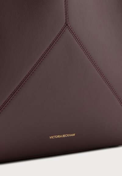 Dark brown leather surface with neat triangular stitching detail and small gold "Victoria Beckham" text near the bottom edge.