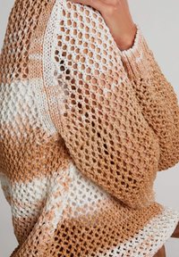 Pull en tricot avec un motif ajouré en treillis dans des tons de beige et crème, avec un fil texturé et des poignets côtelés pour plus de détails.