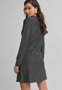 Rochie tricotată gri, cu mâneci lungi, o croială lejeră și un tiv scurt. Textură subtilă și un finisaj neted adaugă un interes vizual.