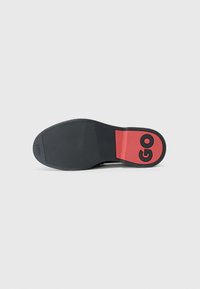 Sort skosål med tekstureret gummioverflade; rød accent med ordet "GO." Kurvet form og logo præget på hælområdet.