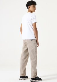 Weißes T-Shirt mit kurzen Ärmeln kombiniert mit hellbeigen, geraden Jeans. Schwarze Sportschuhe runden das Outfit ab. Auffällige Taschen an den Jeans.