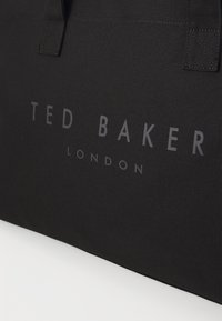 Black textile tote bag featuring the embossed logo "TED BAKER LONDON" in gray. The material has a durable, matte finish and sturdy handles.