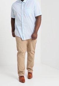 Jasnoniebieska koszula na krótki rękaw z kieszenią na piersi, zestawiona z beżowymi spodniami i brązowymi skórzanymi butami. Prosty design, swobodny krój.