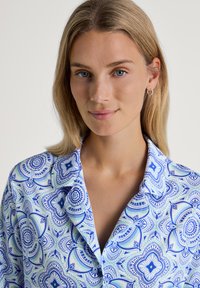 Blue and white patterned shirt featuring floral motifs, collared design, and soft fabric. Close-up view highlights detail and texture.
