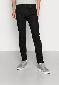 Pantalones vaqueros negros de mezclilla con corte recto, que cuentan con cinco bolsillos y una cintura clásica. Combinados con zapatos deportivos grises.