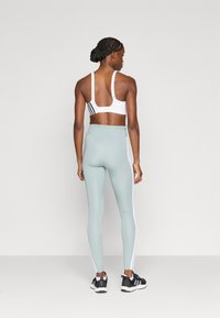 Λευκό αθλητικό σουτιέν με μαύρες ρίγες, συνδυασμένο με ανοιχτόχρωμη  μέντα κολάν με λευκές πλαϊνές ρίγες. Το μοντέλο φοράει μαύρα αθλητικά παπούτσια.