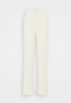 Pantalon en tricot crème avec un motif texturé, doté d'une taille à cordon de serrage et d'un ourlet évasé. Le matériau semble doux et confortable.
