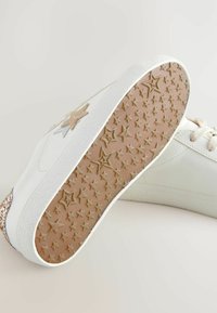 Baskets blanches avec une semelle texturée ornée de motifs d'étoiles ; ornées d'accents en paillettes beiges et d'une semelle en caoutchouc brun clair.