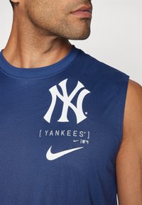 Canotta blu senza maniche con grande logo bianco dei New York Yankees e marchio Nike. Tessuto liscio con scollatura rotonda.