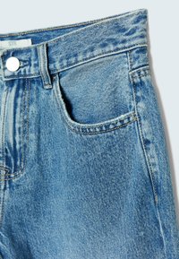 Modré denimové džíny s klasickým střihem, které mají přední kapsu, tónové švy a kovové zapínání blízko pasu.