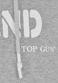 Grå hoodie med stor vit text "TOP GUN" och en flätad dragsko med plastspets. Mjukt, strukturerat material, ledig passform.
