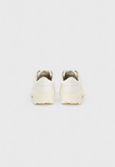 Ζευγάρι λευκά αθλητικά παπούτσια με χοντρή σόλα, σε άποψη από πίσω, σε ανοιχτό γκρι φόντο.