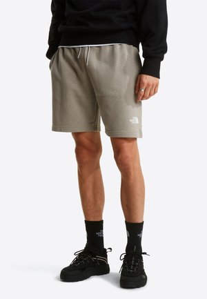 Graue Shorts aus Baumwollmischung mit elastischem Bund, seitlichen Taschen und weißem Logodetail. Kombiniert mit schwarzen Socken und Wanderschuhen.