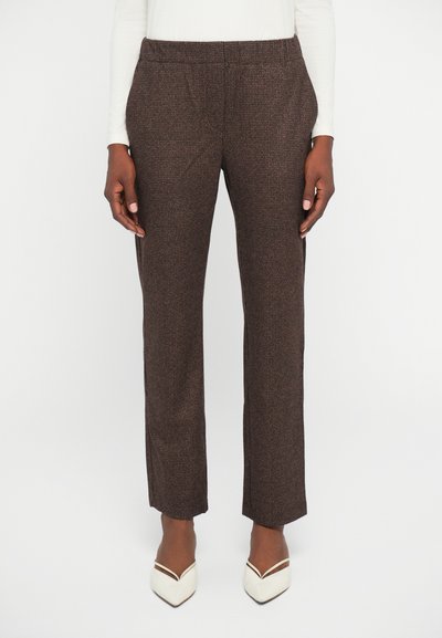 Pantalons marron à motifs avec une coupe droite, poches latérales et taille élastique, associés à des escarpins blancs pointus. Texture lisse.