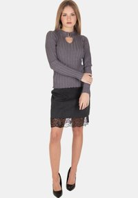 Top grigio a maniche lunghe con righe e scollatura a chiave, abbinato a una gonna nera con orlo in pizzo. La modella indossa tacchi neri.