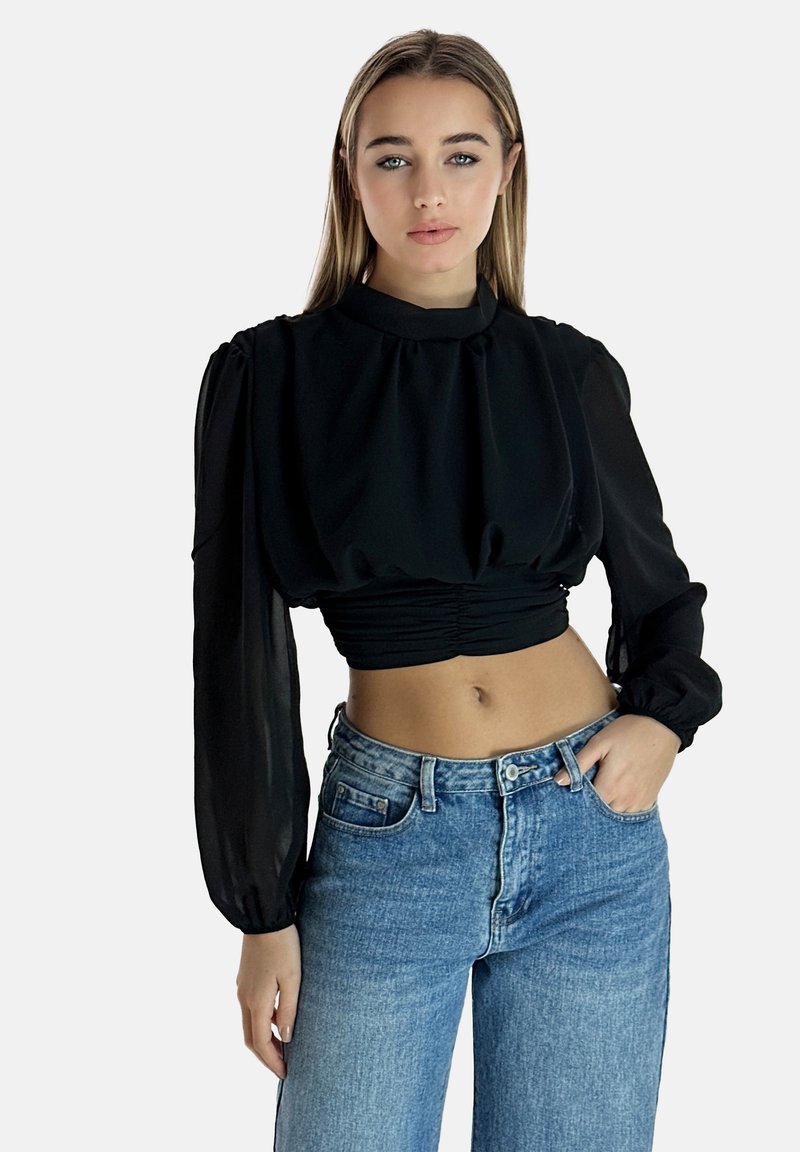 Svart kortärmad blus med puffade långa ärmar, gjord av genomskinlig tyg; draperad design vid midjan. Matchad med högmidjade blå jeans.