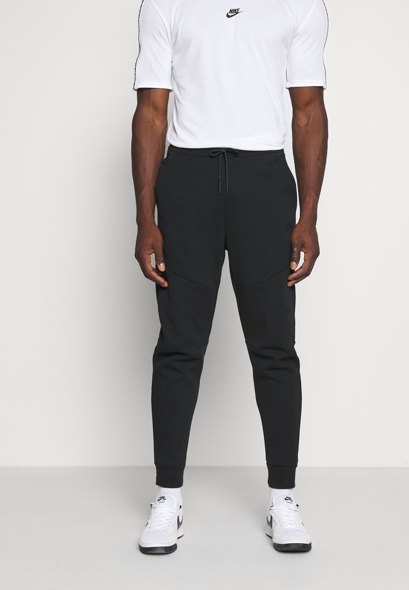 Svarta joggers med texturerat tyg, avsmalnande ben och dragsko i midjan, kombinerade med en vit t-shirt och sneakers.