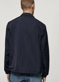 Jachetă ușoară de culoare bleumarin, cu guler, mâneci lungi, manșete elastice și un design simplu. Detaliu vizibil de cusătură la tiv.