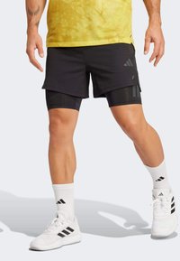 Schwarze Sportshorts mit einem geschichteten Design, die integrierte schwarze Kompressionsshorts darunter haben. Getragen mit weißen Socken und Schuhen.