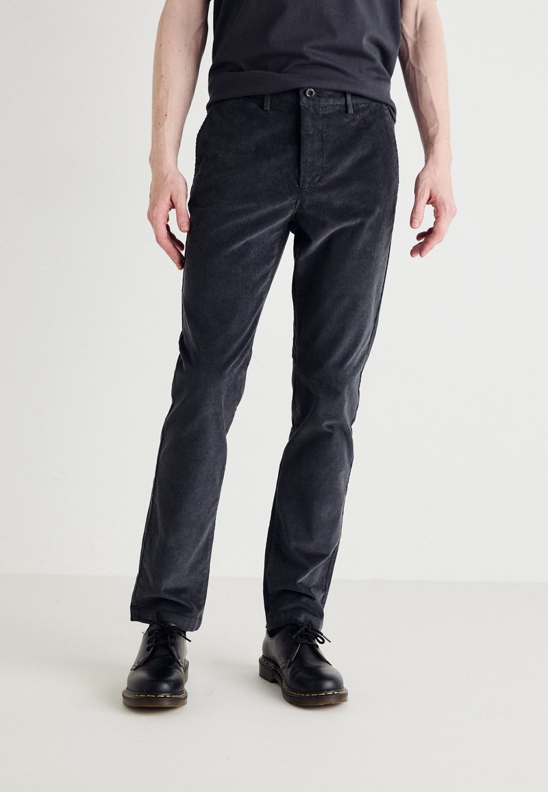 Pantalons en velours côtelé gris foncé avec une coupe slim, dotés d'une fermeture à bouton et à glissière, de poches latérales et d'une texture douce. Des chaussures noires complètent le look.