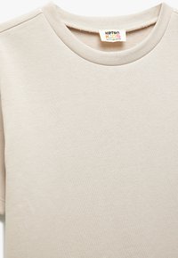 Lys beige kortærmet T-shirt i blød bomuldsblanding. Har en rund hals og subtil ribbet tekstur. Etiket synlig ved halsen.